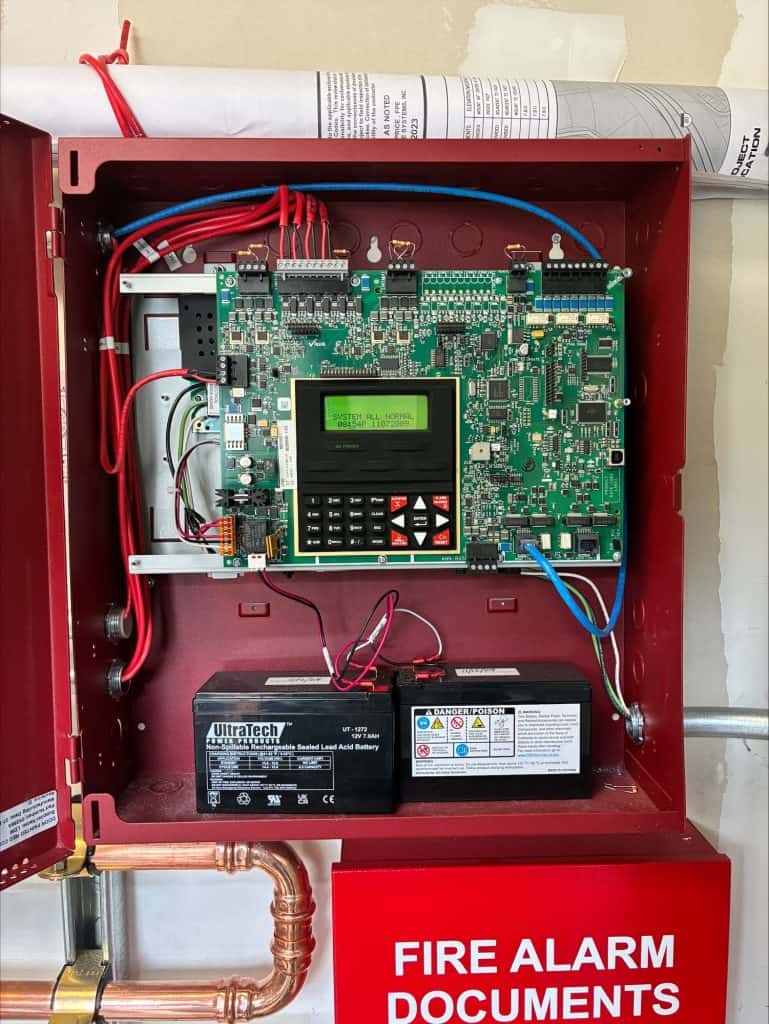 Fire alarm fire alarm system control panel in red metal box with wiring and components.